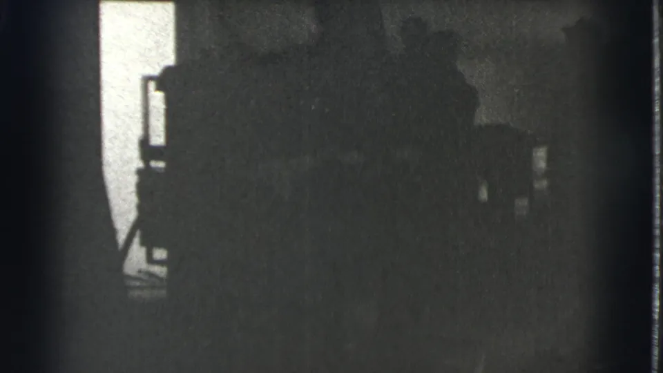 A 1939 Cleveland home-movie frame shows shadowed figures grouped in a low-lit interior, with details mostly obscured by exposure.