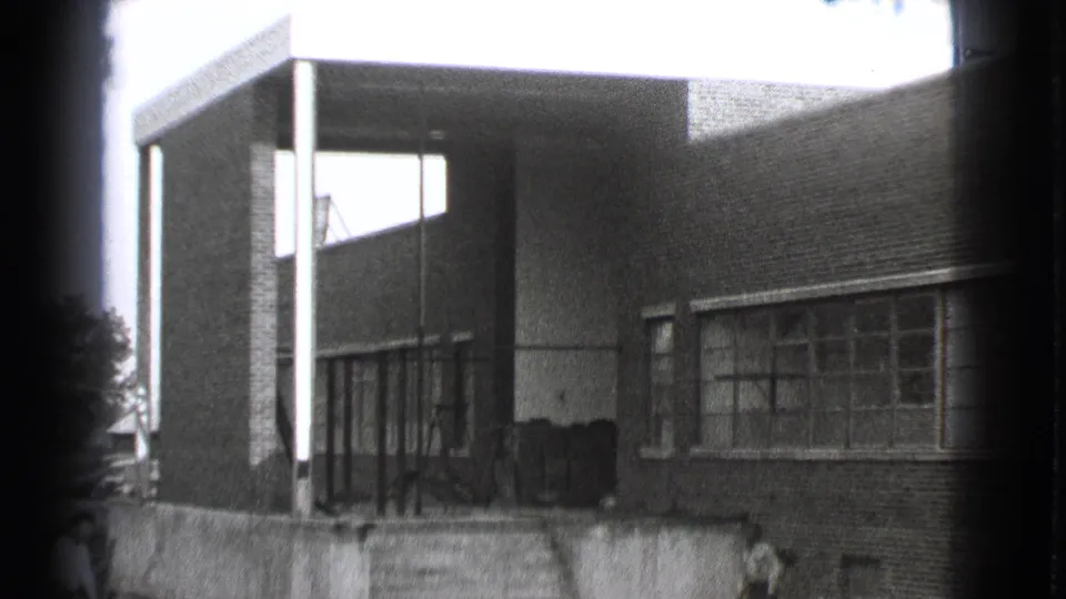 Closer 1939 Cleveland frame showing the brick building facade, window bays, entrance columns, exterior steps, and a man near the wall.