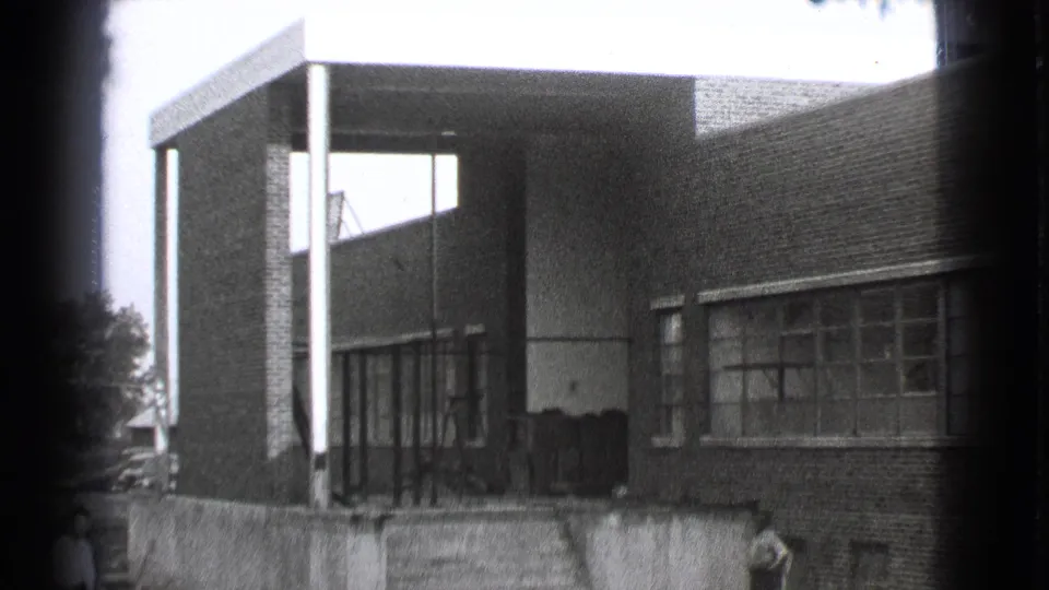 1939 Cleveland home-movie frame showing a modern brick building with a covered entrance, vertical columns, large windows, and people near the lower edge.