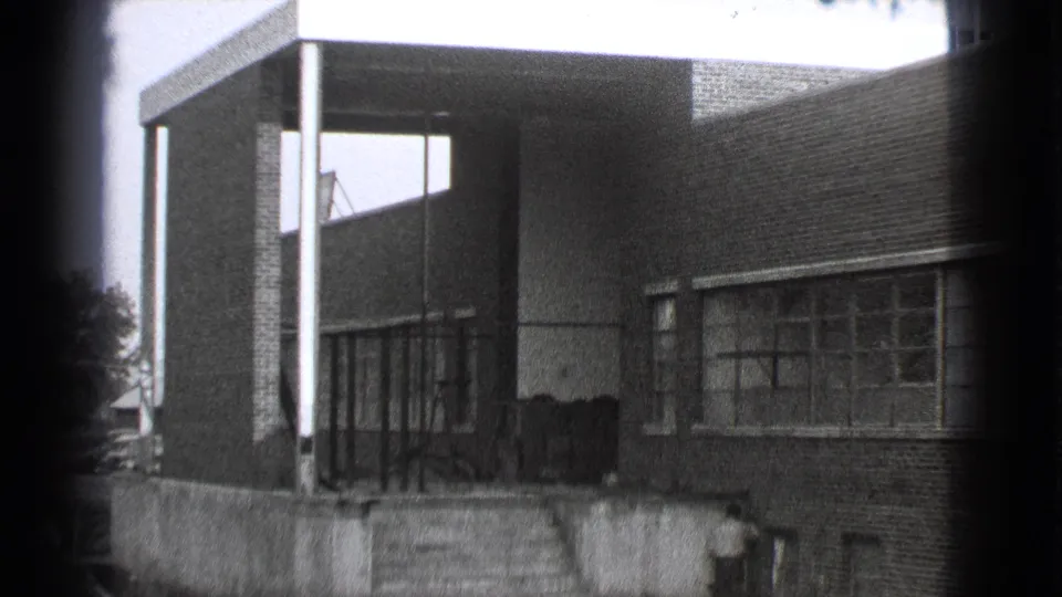 Final 1939 Cleveland frame of the brick building exterior, showing the entrance columns, broad windows, lower wall, and a partly visible person at the bottom edge.