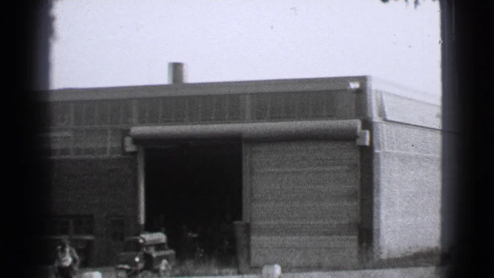 1939 Cleveland industrial exterior with a garage bay, small truck, and worker figure near the factory wall.