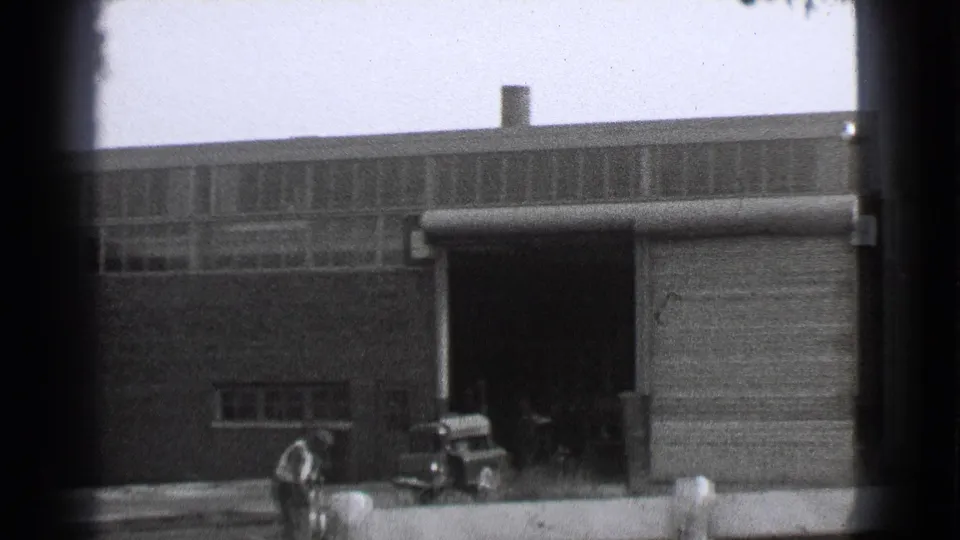 Cleveland factory exterior from 1939 showing a worker near a small truck outside an open garage door.