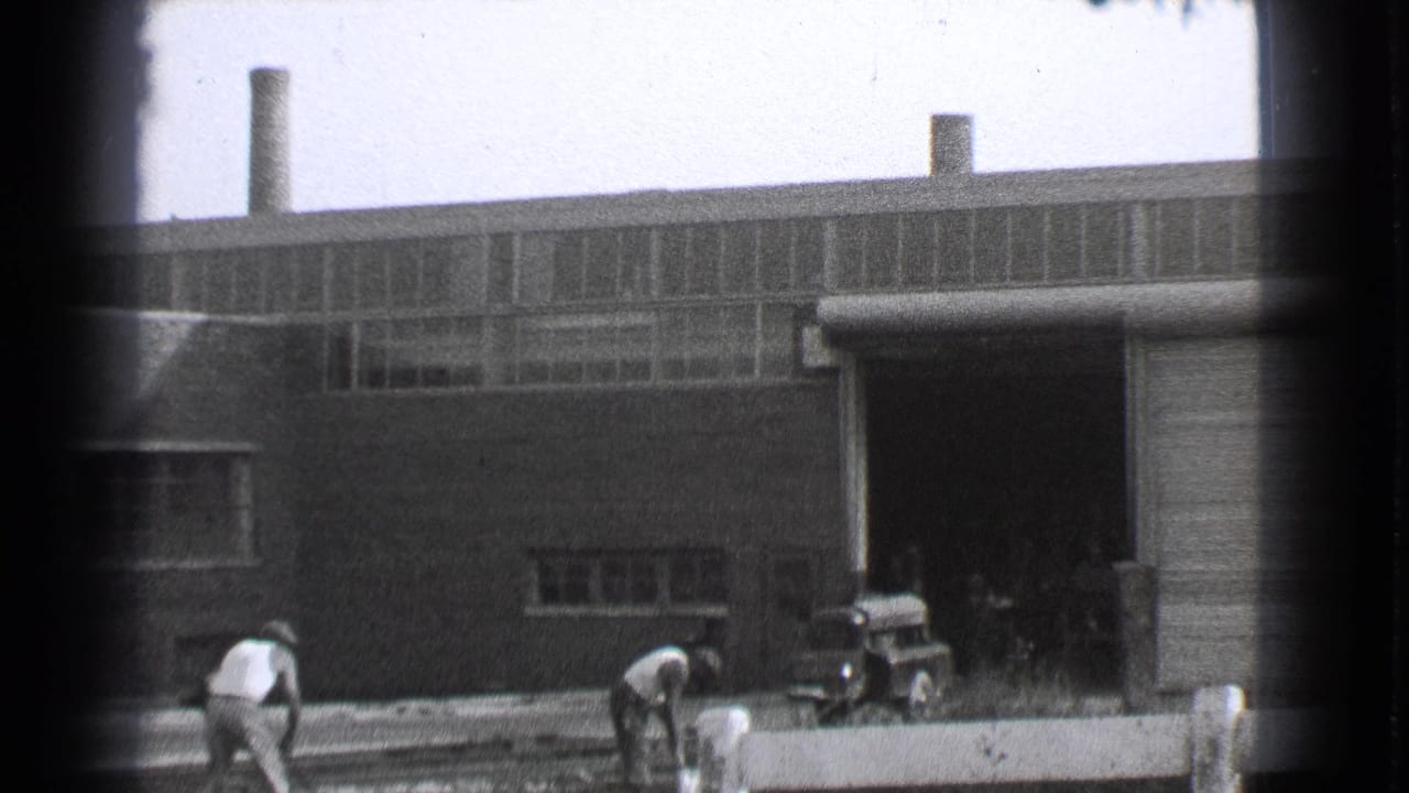 1939 Cleveland 8mm frame showing men working near railway tracks outside a large brick factory building.