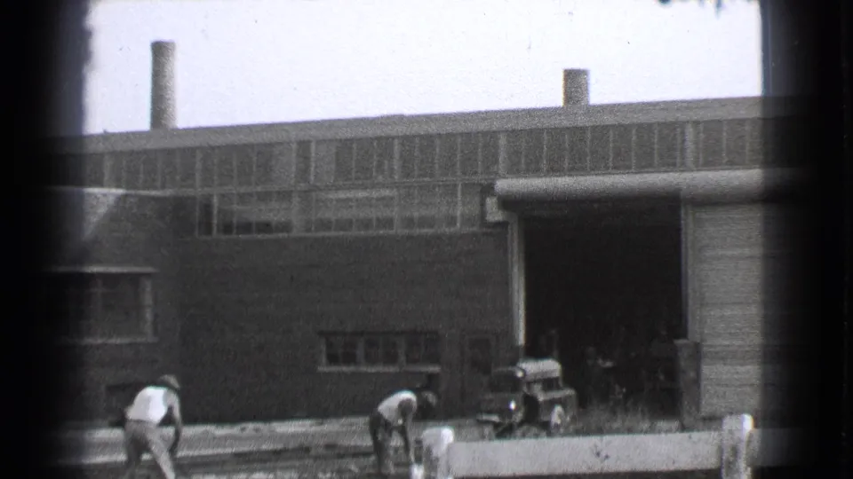 1939 Cleveland 8mm frame showing men working near railway tracks outside a large brick factory building.