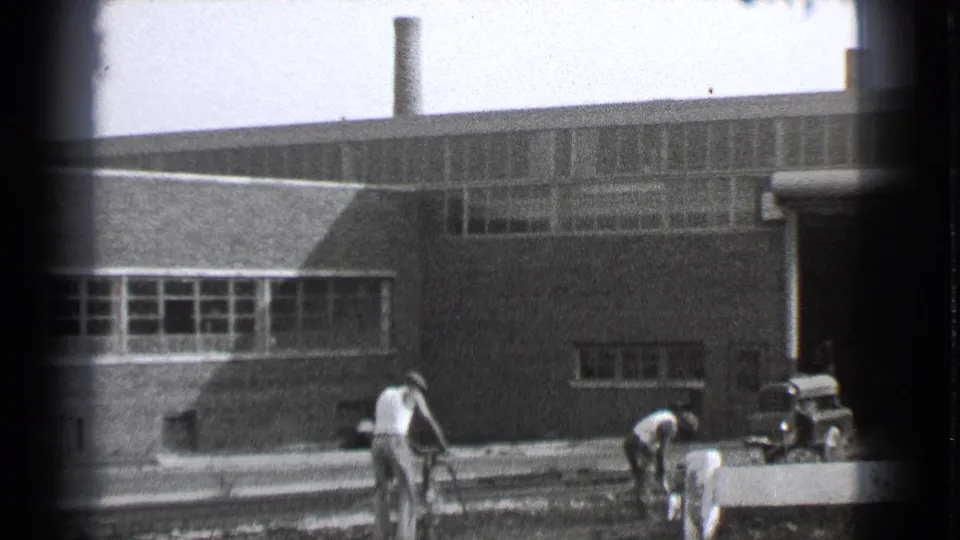 Cleveland factory exterior with workers using tools near railway tracks and a small truck parked nearby.