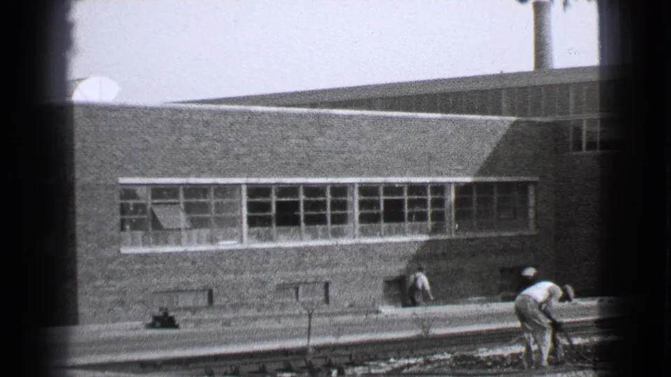 1939 Cleveland industrial yard scene with workers near rails and a brick factory facade behind them.