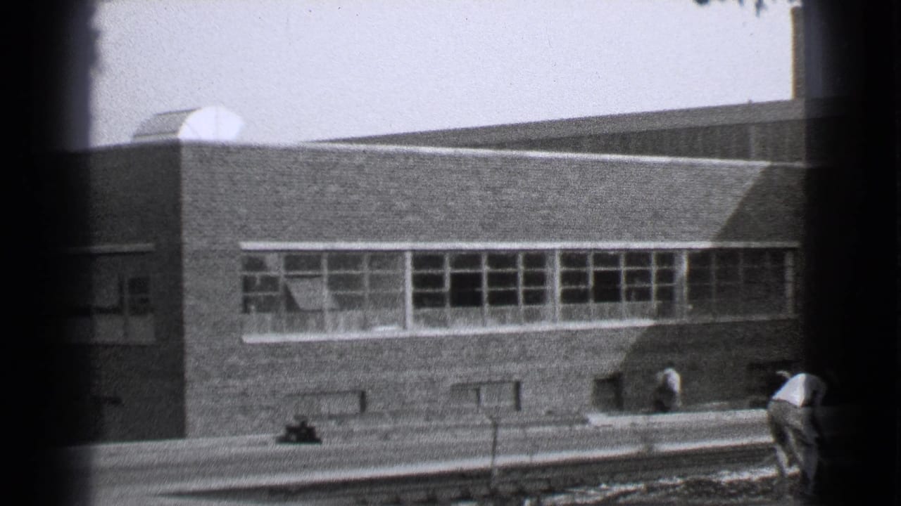 Brick building with rows of small windows seen from street level.