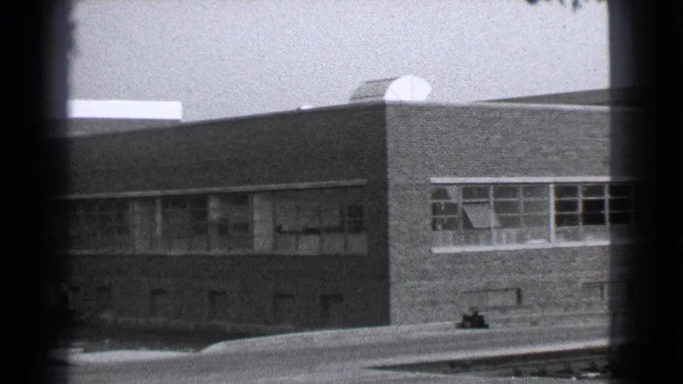 1939 Cleveland home-movie frame showing an angled brick facade, small windows, flat roof, and street foreground.