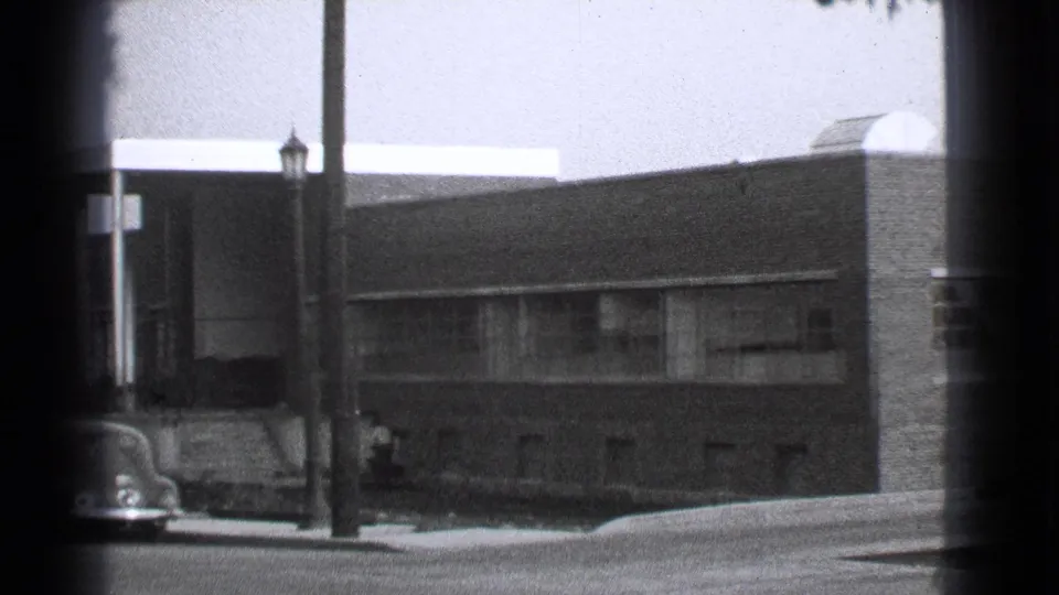 1939 Cleveland frame showing the brick building, a street pole, a distant pedestrian, and part of an older car at the lower left.