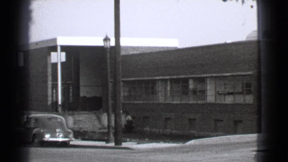 1939 Cleveland street view with a brick institutional or apartment building, parked rounded sedans, sidewalk, and foreground lamppost.