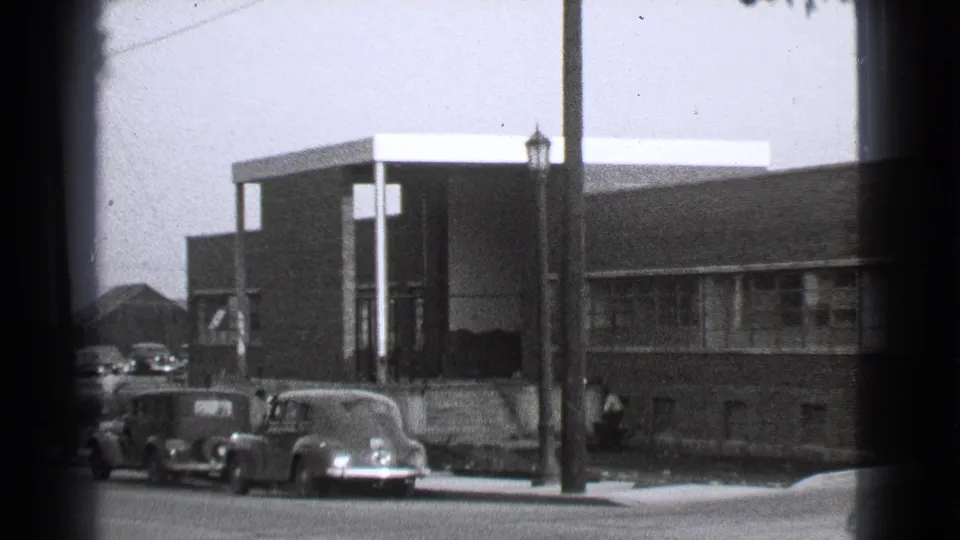 Cleveland, 1939, with late-1930s cars parked near a modern brick building, a lamppost, and a small figure by the sidewalk.