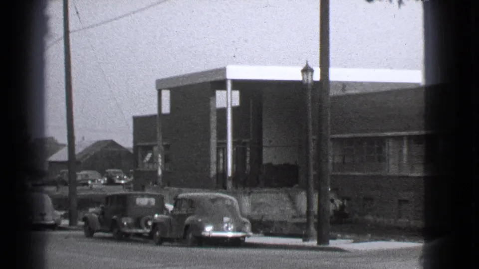 1939 Cleveland exterior view with curbside automobiles, a foreground lamppost, sidewalk figures, and a brick school or apartment-like building.