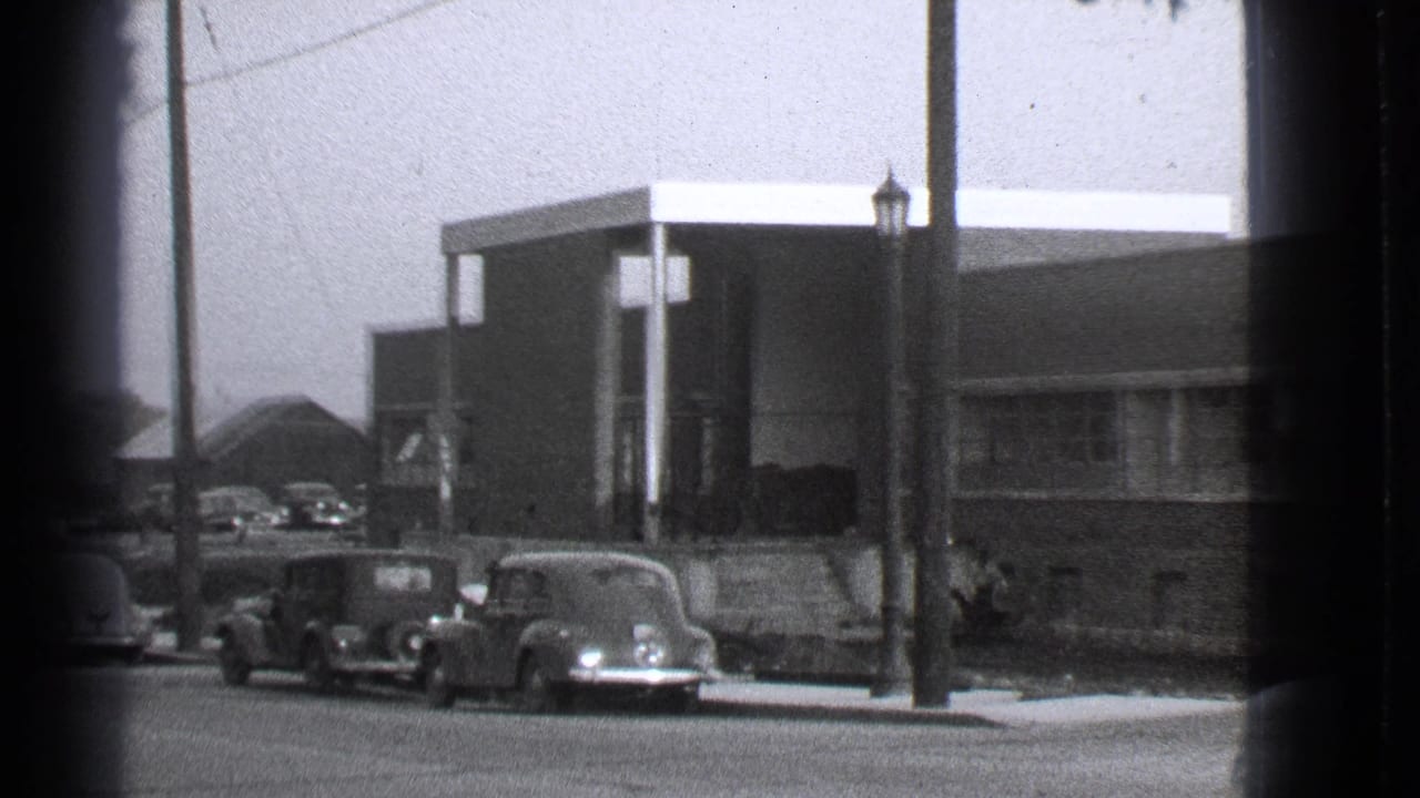 Parked classic cars along a street outside a low modern building.