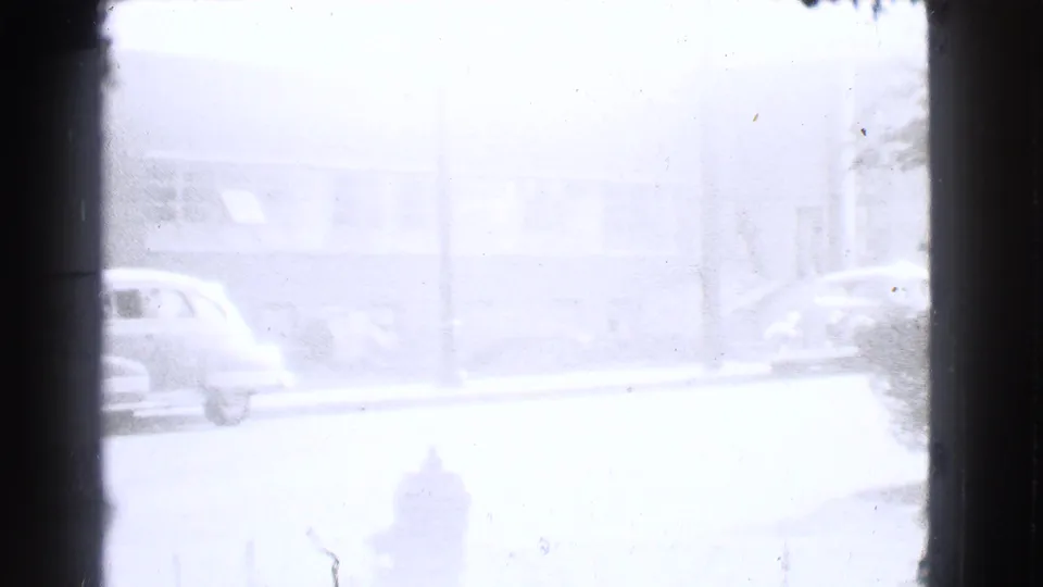 Soft, overexposed 1939 Cleveland street frame showing a parked car, fire hydrant, and building facade beyond the road.
