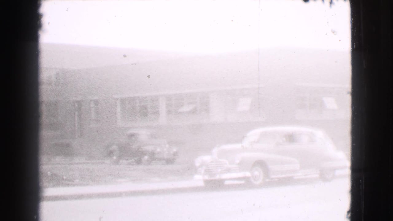 Parked sedans and a small truck outside a low windowed building.