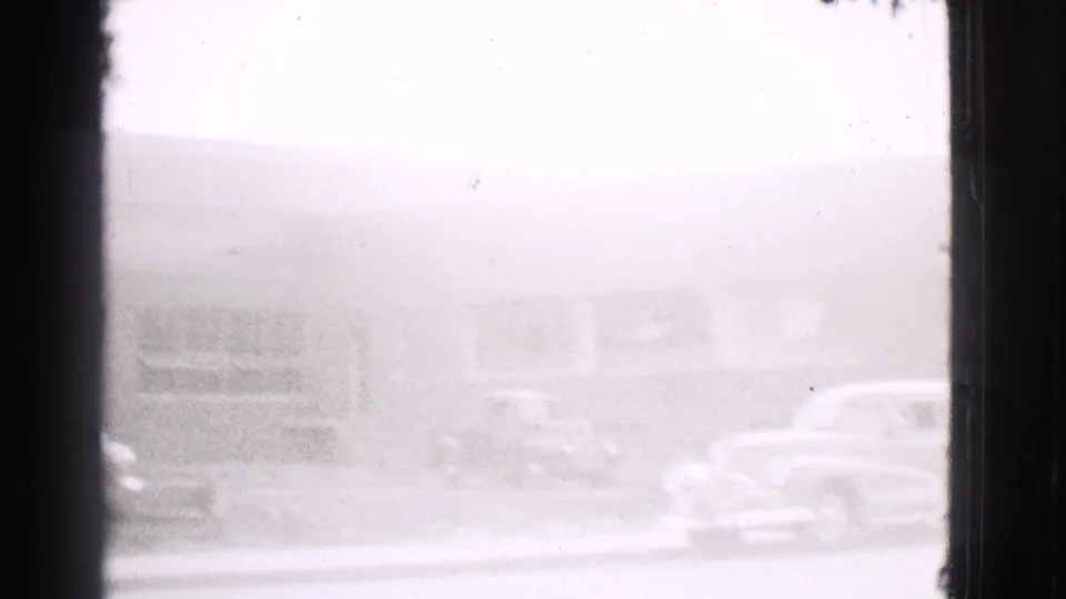Soft 8mm frame from the Cleveland street pan, showing parked cars beside a low building in 1939.