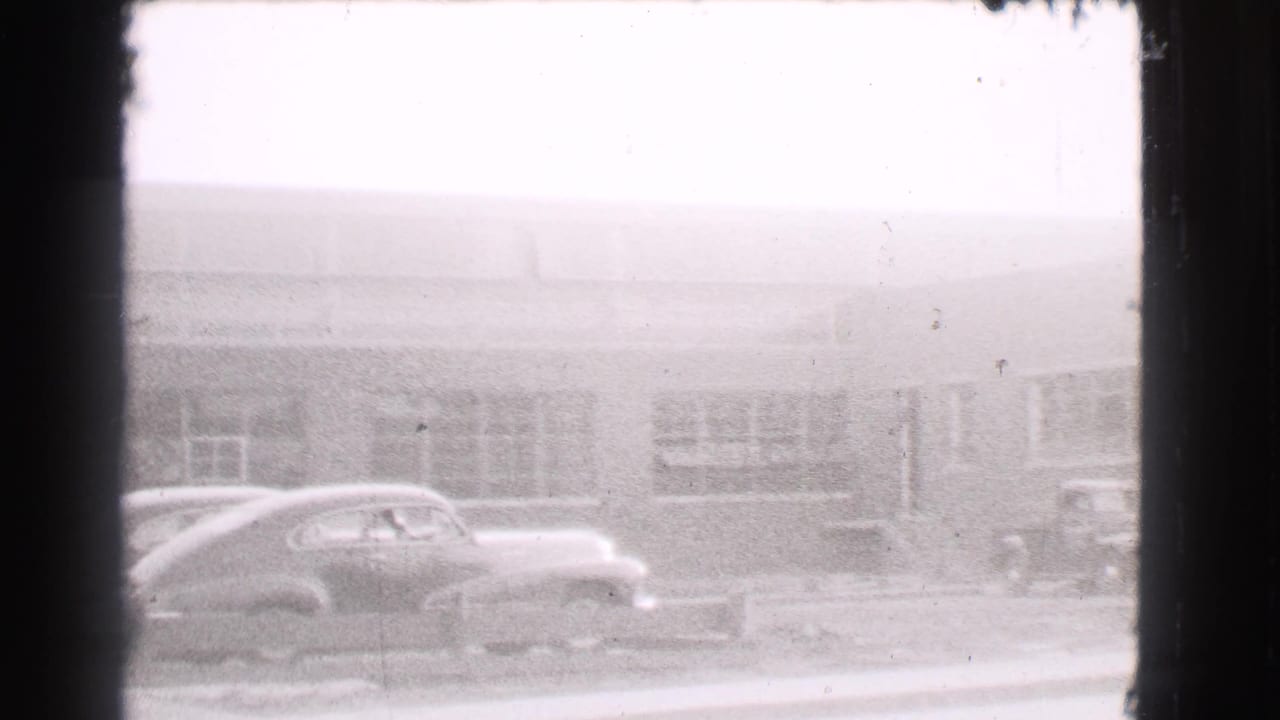 Rounded sedan parked along the curb in front of a long building with large windows.