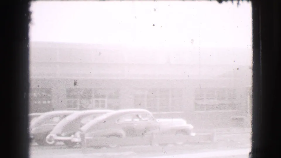 Multiple late-1930s cars are parked along a Cleveland street, partly washed by exposure and film grain.