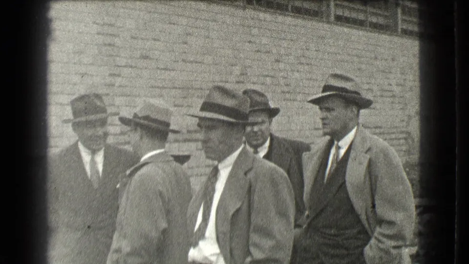 The group of men remains outside the brick building, with several faces and fedora-style hats visible in the 1939 Cleveland footage.