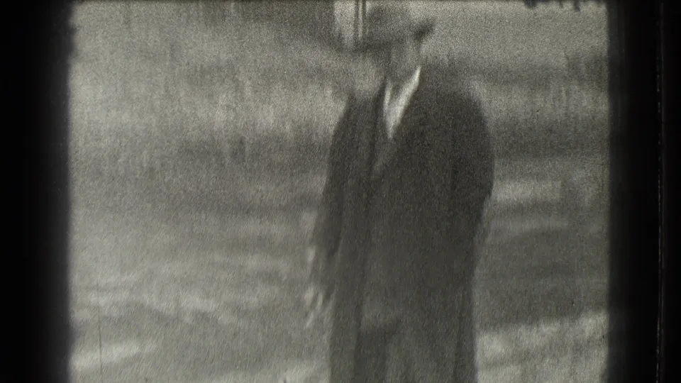 A single adult man in a dark suit and brimmed hat stands alone in soft focus near the end of the 1939 Cleveland home-movie clip.