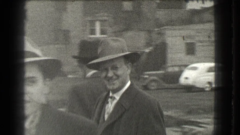 Several adult men in suits and hats gather near unpaved ground and parked cars in the 1939 Cleveland home-movie scene.