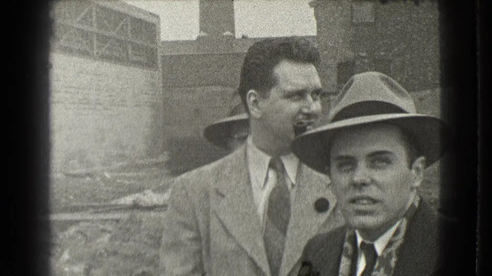 Two suited men appear near the camera in Cleveland, with one fedora-wearing man in front and another man standing behind him.