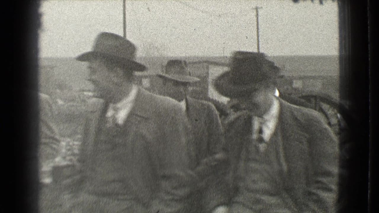 Several men in hats and overcoats walking outdoors near industrial equipment.