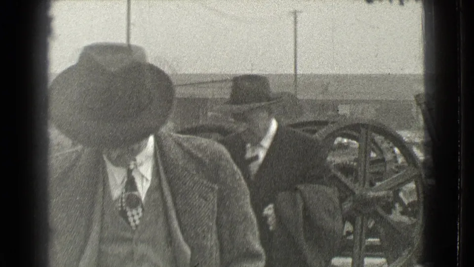 A close view from the 1939 Cleveland home movie shows a man in a fedora and overcoat passing in front of industrial wheels.