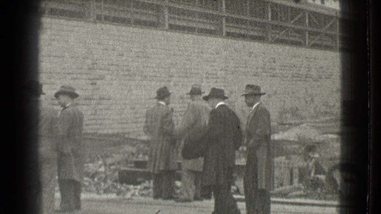 Men in suits and hats stand near a brick wall at a construction site.