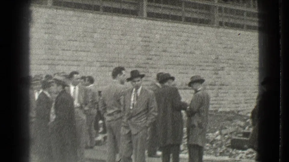 A closer cluster of men in suits and hats stands at the Cleveland construction site, with scattered rubble visible behind them.