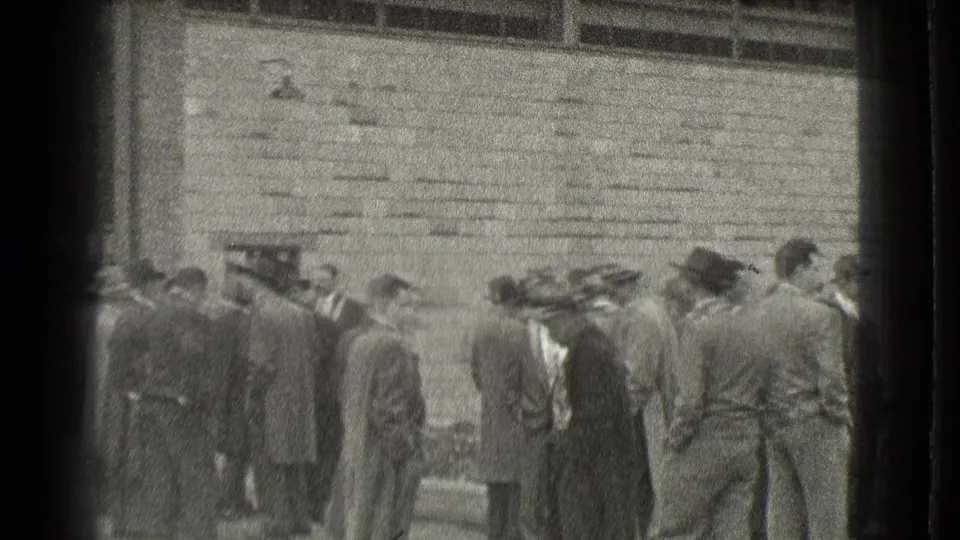 In 1939 Cleveland footage, men in suits, coats, and brimmed hats stand outside a masonry building entrance.