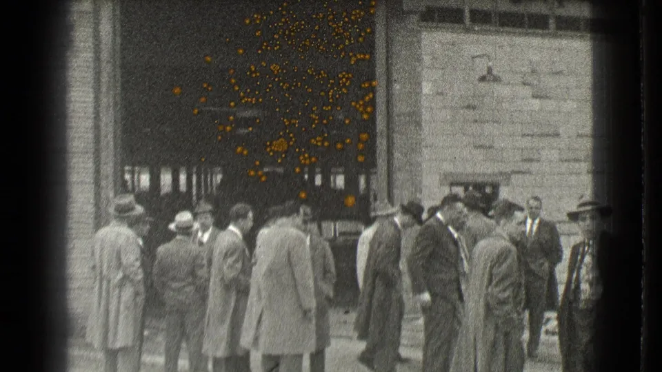 A sidewalk group of formally dressed men stands near a Cleveland building entrance, with part of a car at the edge.
