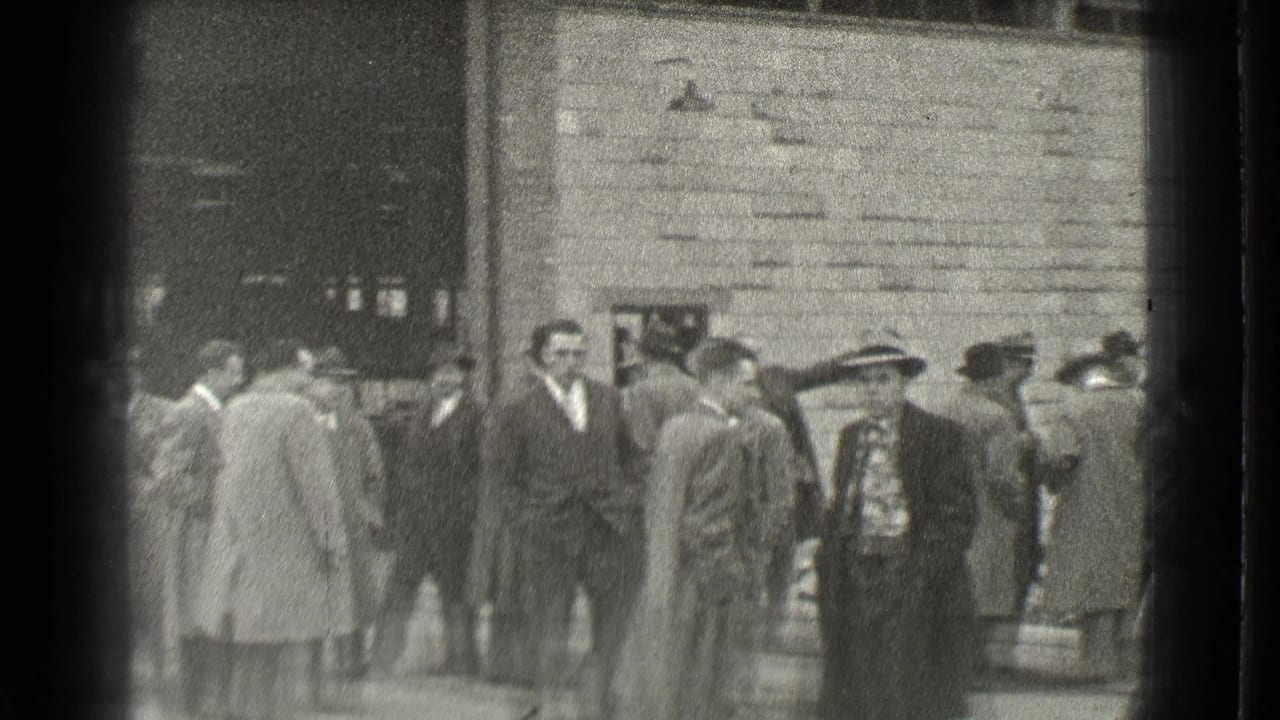 In Cleveland, Ohio in 1939, adult men in suits, overcoats, and hats appear to wait or talk outside a brick or stone building.