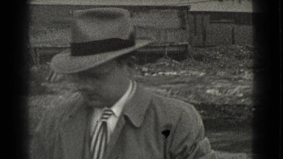 A man in a fedora, coat, and striped tie passes close to the camera in the 1939 Cleveland home-movie scene.
