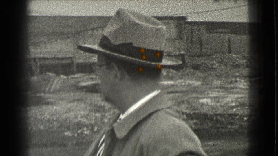 A man in period hat and coat is seen in profile in Cleveland, Ohio, with masonry and uneven ground behind him.