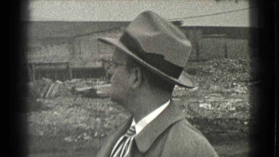 A fedora-wearing man is shown from the back and side in the 1939 Cleveland street scene, with wall and ground textures behind him.
