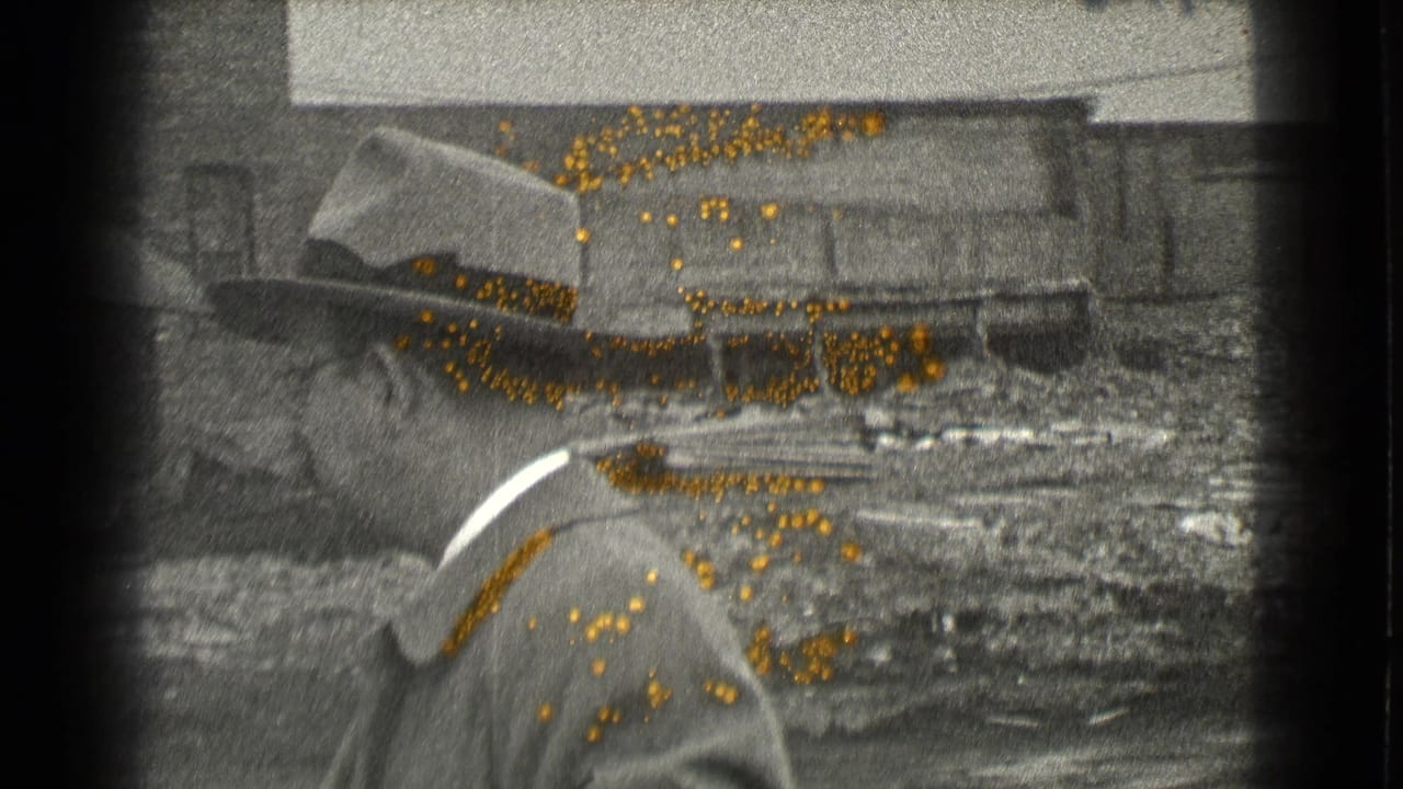 Man in fedora and suit seen in profile before an industrial yard.