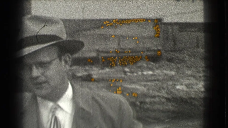 A man in a suit, tie, glasses, and fedora faces slightly toward the camera in a 1939 Cleveland industrial setting.