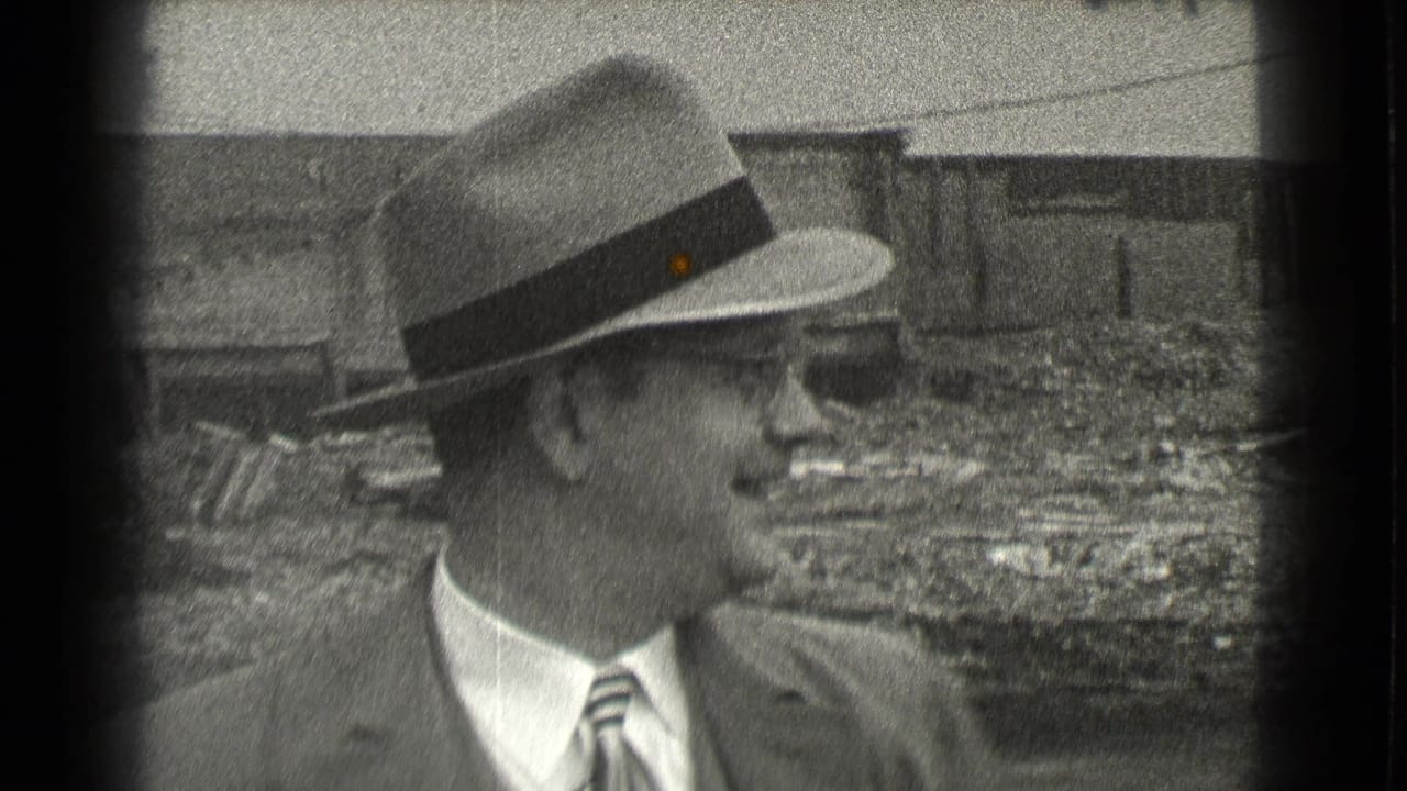 Suited man in a fedora and glasses standing before an unfinished construction area.