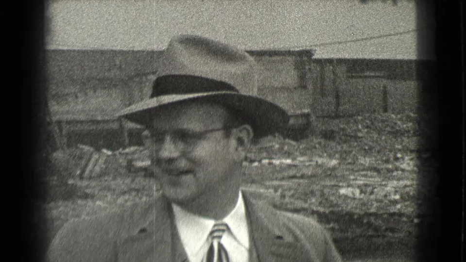 A smiling suited man in a fedora appears in the foreground of the Cleveland construction scene, with rubble and unfinished walls behind him.