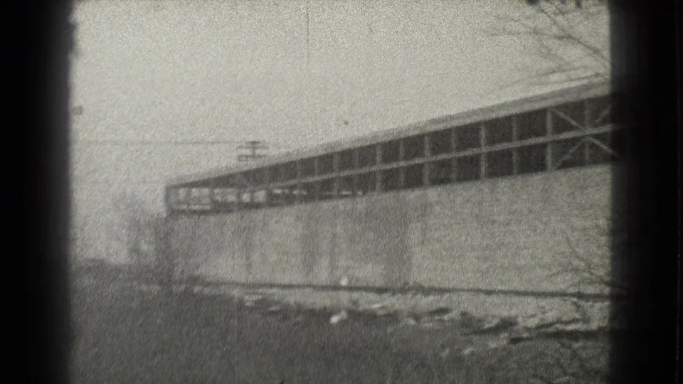 1939 Cleveland 8mm frame showing a large brick warehouse exterior with a long upper window band, bare branches, and patchy snow near the wall.
