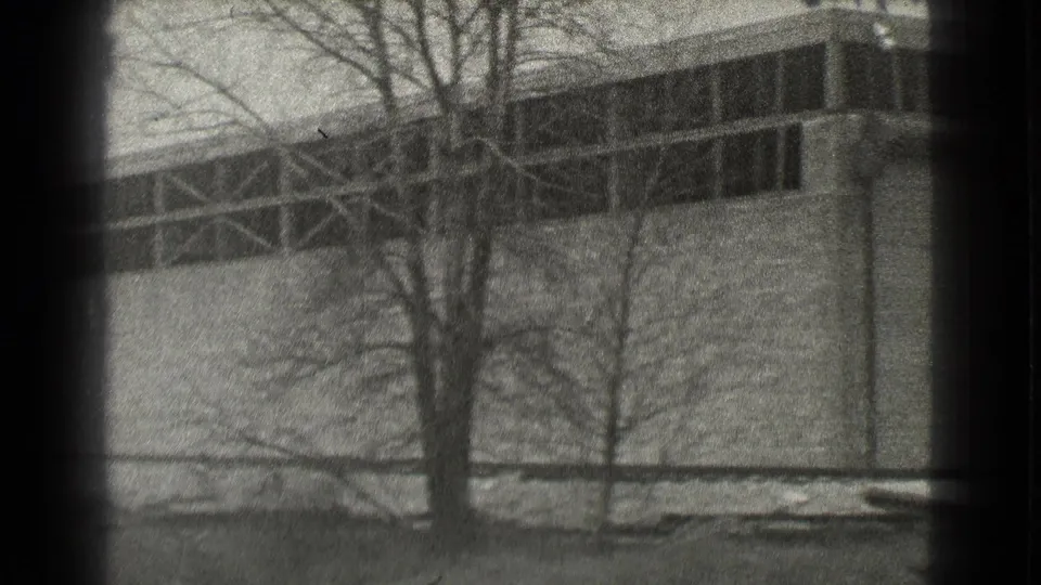 1939 Cleveland 8mm frame with bare trees crossing the view of a brick industrial wall and dark upper window bays.