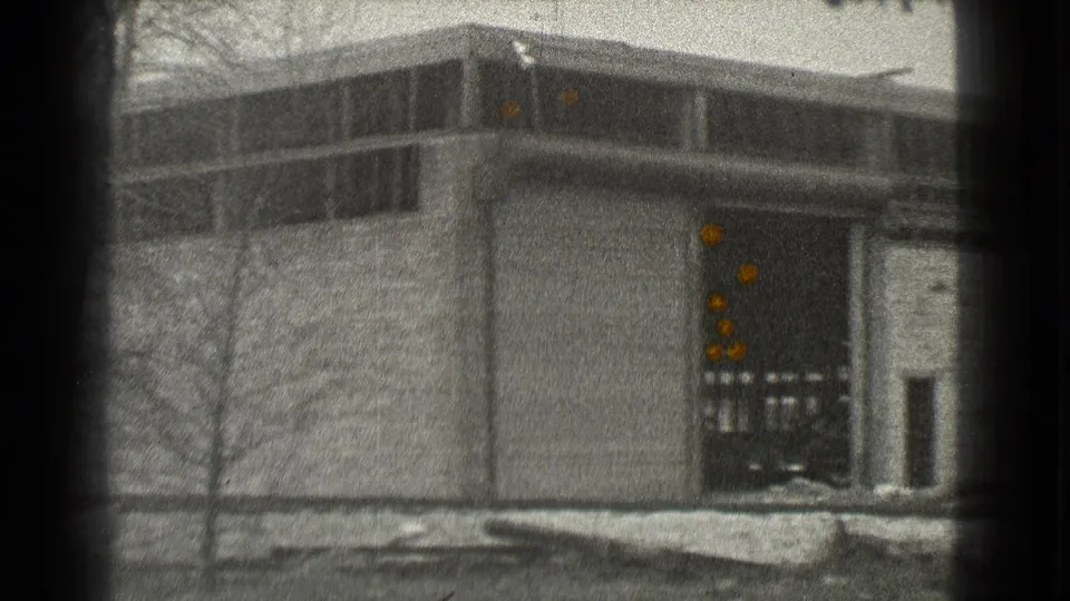 1939 Cleveland frame showing a warehouse corner, elevated window band, loading dock doorway, bare trees, and snow patches in the foreground.