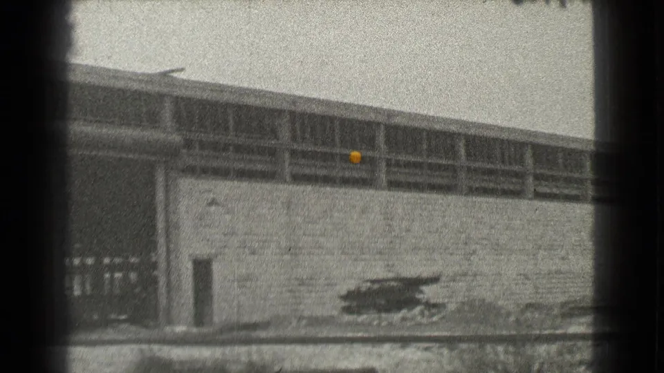 Black-and-white 1939 Cleveland frame of the factory wall, open bay area and scattered material near the exterior.