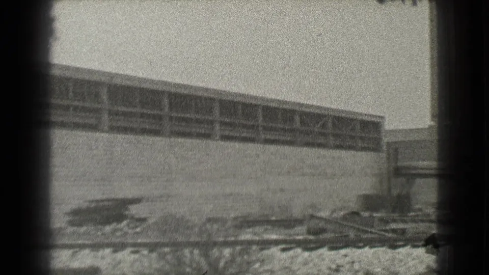1939 Cleveland 8mm view of a long industrial wall, high windows and rough ground with debris in front.