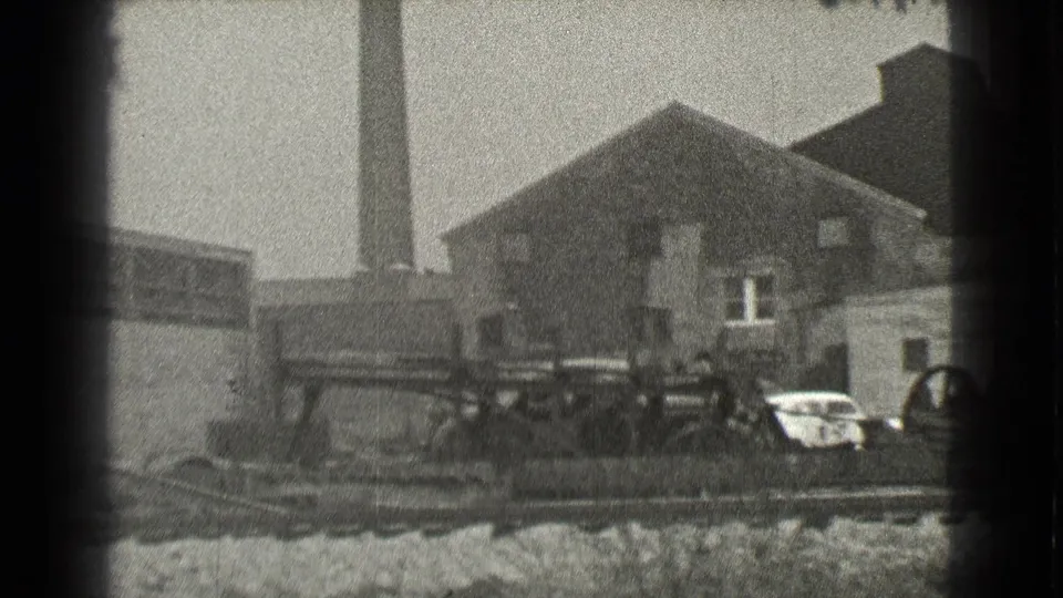 1939 Cleveland industrial yard with rail tracks, a tall smokestack, brick buildings, debris, and parked automobiles.