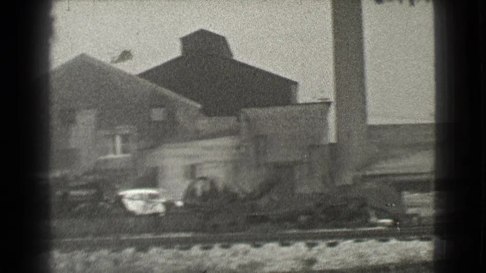 Black-and-white 1939 Cleveland view of a brick industrial structure, parked cars, rail tracks, and debris in the foreground.