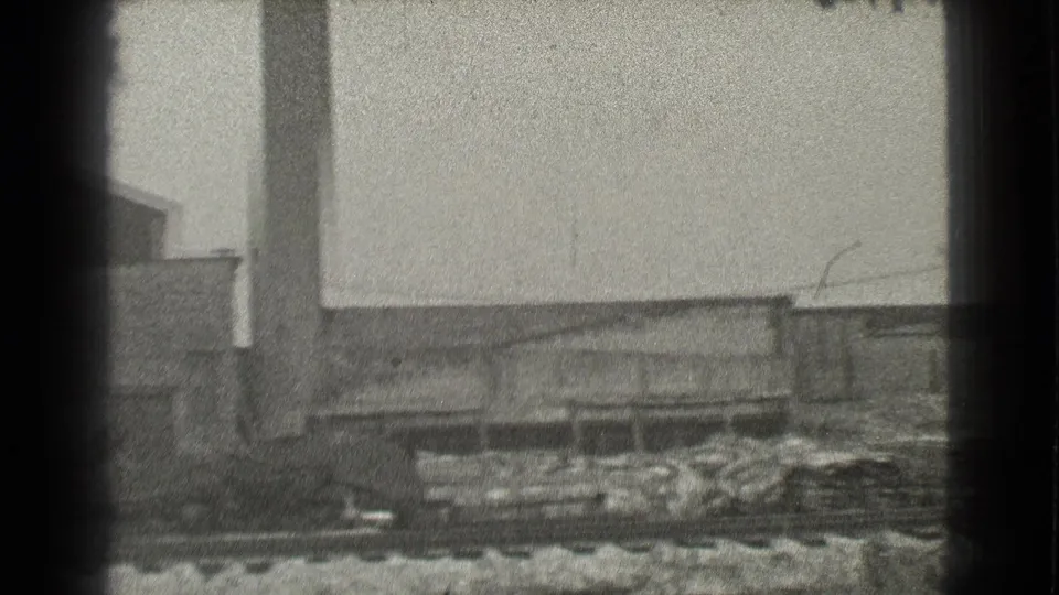 1939 Cleveland industrial exterior with a tall smokestack, low buildings, rail tracks, and discarded materials in the yard.