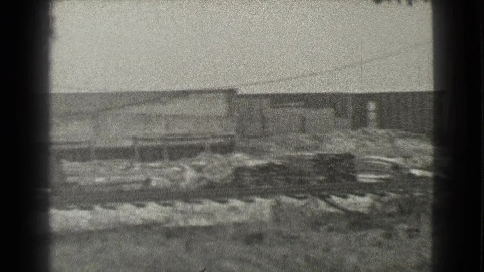 Black-and-white 8mm frame of Cleveland industrial buildings with piles of material along the foreground.