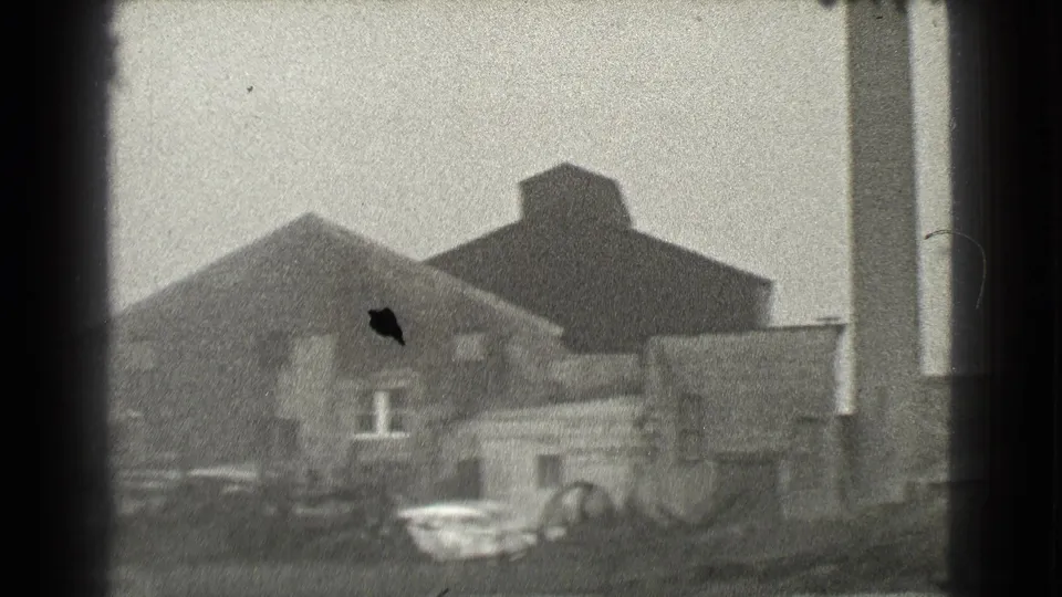 Cleveland industrial building exterior on 8mm film, with a parked car and adjacent structures visible.